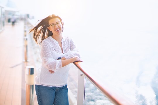 Young beautiful woman on vacation smiling happy and confident. Standing on a deck of ship with smile on face doing a cruise