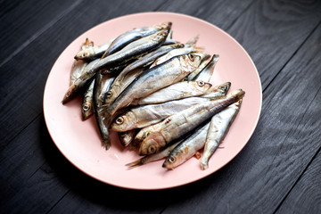 Raw fish sprats, herring on a plate on a dark wooden background.