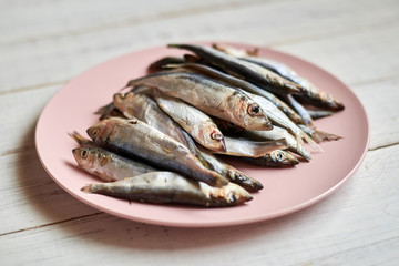Raw fish sprats, herring on a plate on a light wooden background.