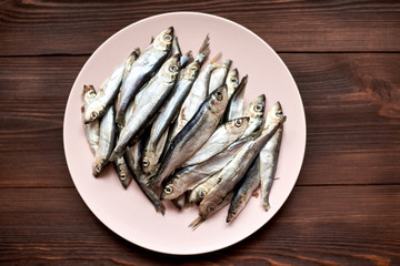 Raw fish sprats, herring on a plate on a wooden background.