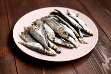 Raw fish sprats, herring on a plate on a wooden background.