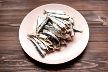 Raw gutted fish sprats, herring on a plate on a wooden background.