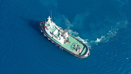 Aerial drone top down photo of tug boat cruising in industrial carrier logistics terminal