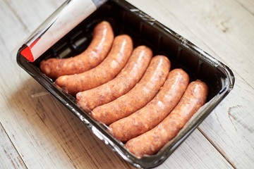 Raw sausages for grill in packaging on a light wooden background.