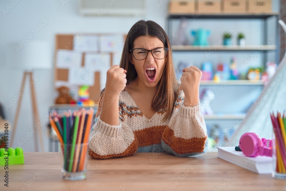 Sticker young beautiful teacher woman wearing sweater and glasses sitting on desk at kindergarten angry and 