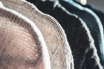 Collection of warm sweaters hanging on rack against graybackground, closeup