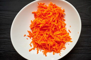 Grated carrots in a white plate on a dark wooden background.
