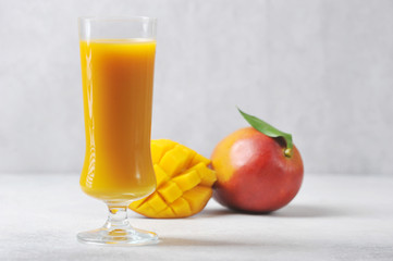Mango juice in a tall glass.  The whole Mango and half of the fruit complete the composition.  Light background.  Close-up.