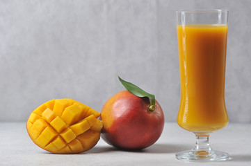Mango juice in a tall glass.  Next to the glass is a whole Mango and half of the fruit.  Light background.  Close-up.