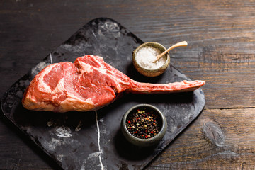 Raw Tomahawk steak on wooden background with spices for grilling, top view, copy space