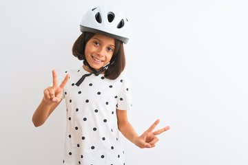 Beautiful child girl wearing security bike helmet standing over isolated white background smiling looking to the camera showing fingers doing victory sign. Number two.