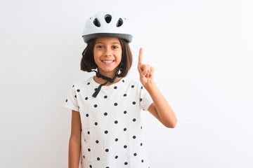 Beautiful child girl wearing security bike helmet standing over isolated white background showing and pointing up with finger number one while smiling confident and happy.