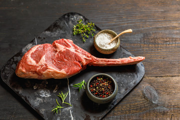 Raw Tomahawk steak on wooden background with spices for grilling, top view, copy space