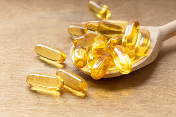 Cod liver oil omega 3 gel capsules on a spoon on wooden background.