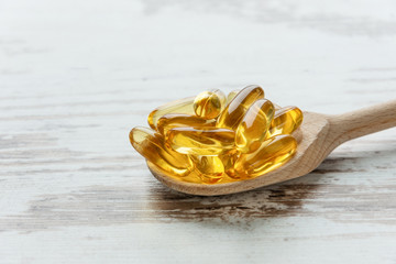 Cod liver oil omega 3 gel capsules on a spoon on wooden background.