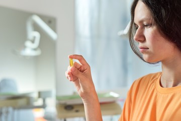Teenage girl holding yellow vitamin d gel capsule in hand, dentist office background