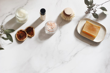 Styled beauty frame. Handmade soap bar, shampoo bottle, dry eucalyptus, lemons, wooden brush and Himalayan salt. White marble table background. Organic cosmetics, spa concept. Flat lay, top view.