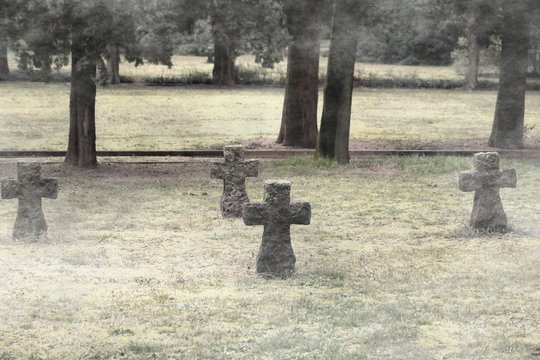 Graveyard with old medieval gravestone in shape of cross on the meadow in the cloudy and cold winter day. Photo in sepia color technique