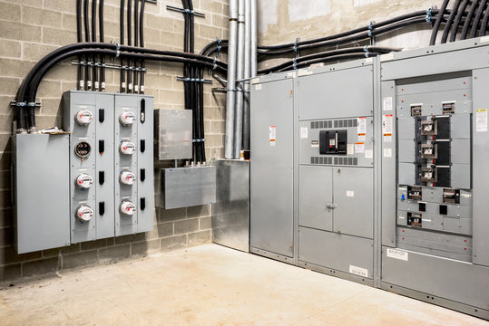 Electrical room of residential or commercial building. Multiple smart meters, main power breaker, meter stacks and cabinets. Perspective view