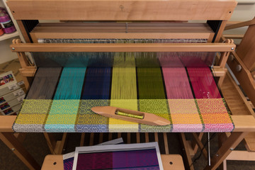 Partly completed woven fabric on a loom with a shuttle resting on the material.