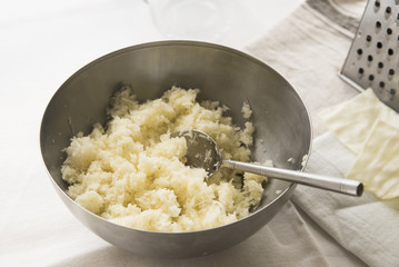 A semicircular metal bowl with grated white cabbage and a spoon for making salad.