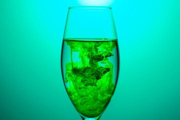 green food coloring diffuse in water inside glass , with blue background