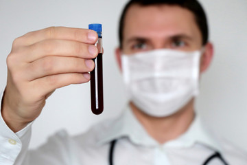 Test tube in male hand close up, doctor in medical mask holding a vial with red liquid. Concept of...
