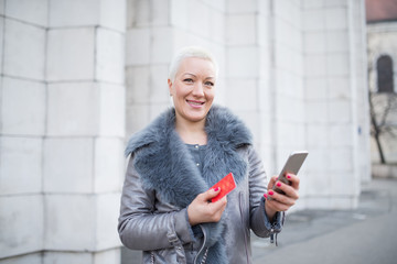 Woman on the street uses a cellphone and holding payment card