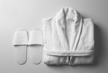 Clean folded bathrobe and slippers on white background, flat lay