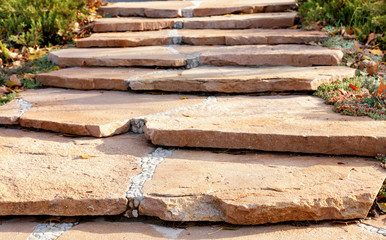 A paved path made of coarse sandstone in a beautiful park, framed by a low shrub in the rays of...