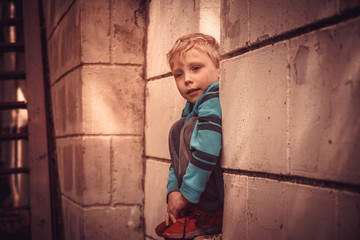The blond European boy is sad. The child is sitting on a stone fence and is bored.