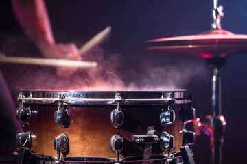 The drummer plays the drums. Beautiful blue and red background, with rays of light. Beautiful special effects smoke and lighting. The process of playing a musical instrument. Close-up photo.