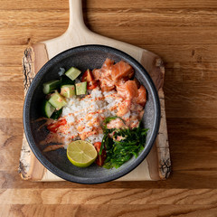 Raw salmon poke bowl with white rice, chuka and cucumber on wooden rustic table