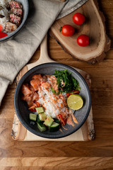 Raw salmon poke bowl with white rice, chuka and cucumber on wooden rustic table