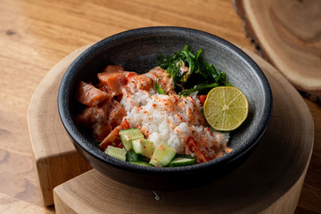 Raw salmon poke bowl with white rice, chuka and cucumber on wooden rustic table