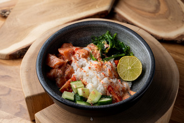 Raw salmon poke bowl with white rice, chuka and cucumber on wooden rustic table