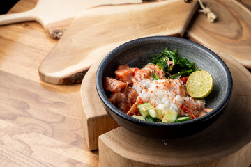 Raw salmon poke bowl with white rice, chuka and cucumber on wooden rustic table
