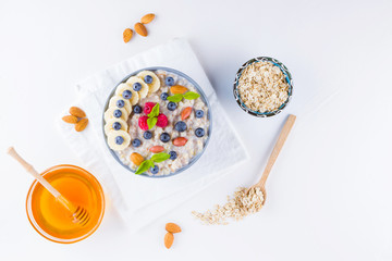 Healthy breakfast. Oatmeal with blueberries, banana and raspberry. Oatmeal with fruits and nuts in a bowl. Cooked oatmeal and honey on white background. Vegetarian food. Copy space