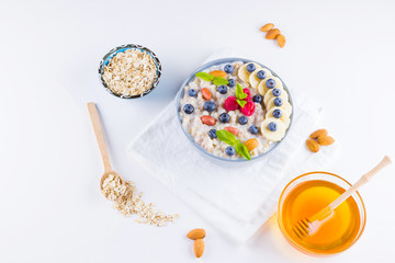 Healthy breakfast. Oatmeal with blueberries, banana and raspberry. Oatmeal with fruits and nuts in a bowl. Cooked oatmeal and honey on white background. Vegetarian food. Copy space