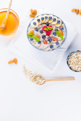 Healthy breakfast. Oatmeal with blueberries, banana and raspberry. Oatmeal with fruits and nuts in a bowl. Cooked oatmeal and honey on white background. Vegetarian food. Copy space