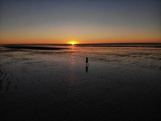 Girl in a dress standing at the beach during beautiful orange sunset on eighty mile beach  with the reflecting sun in Western Australia, Australia