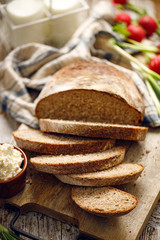 Traditional sourdough loaf of bread cut into slices and curd cheese on a wooden board, close up. 