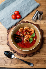 Hot and spicy tomato soup with king prawns, scallops and garlic, on wooden rustic table, top view