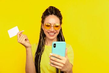 Pretty young lady in bright clothes watching camera and posing with blue phone and credit card