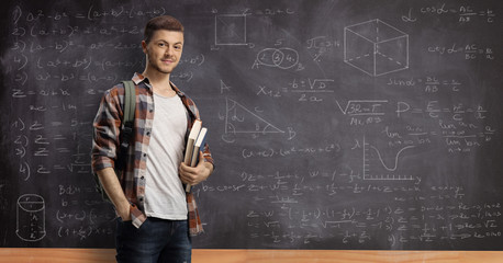 Male student posing in front of a blackboard with math formulas and equations - obrazy, fototapety, plakaty