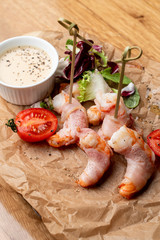 Close up of roasted shrimps wrapped in bacon with sauce and green salad