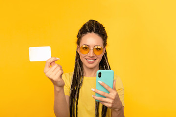 Pretty young lady in bright clothes watching camera and posing with blue phone and credit card