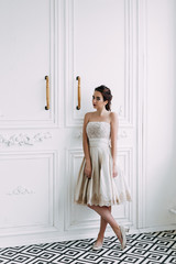 Beautiful slender girl with dark hair in a light dress in a white interior