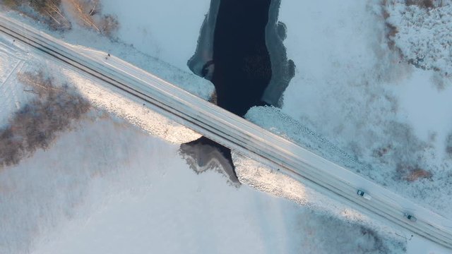 Aerial top down view of cars driving across snowy road through bridge crossing a icy water lake during sunset winter time. Cool, cold, clear and fresh weather. Finland, J&auml;ms&auml;, Himos