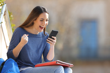 Excited student checking smart phone content in a campus